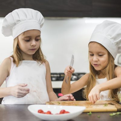 little-kid-assisting-her-sister-cut-vegetables-with-knife